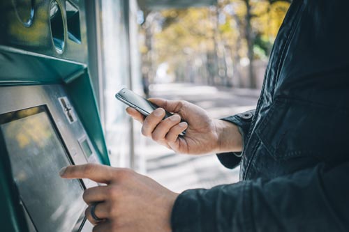 Customer using an ATM machine while holding mobile phone.